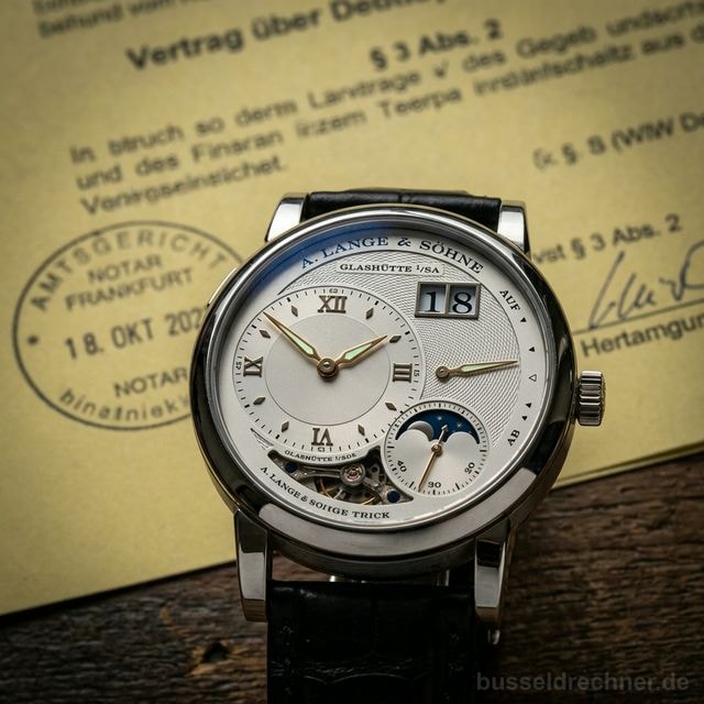 Makroaufnahme eines luxuriösen mechanischen Chronographen, der die Zeit misst, mit einem gelben deutschen Rechtsdokument unscharf im Hintergrund